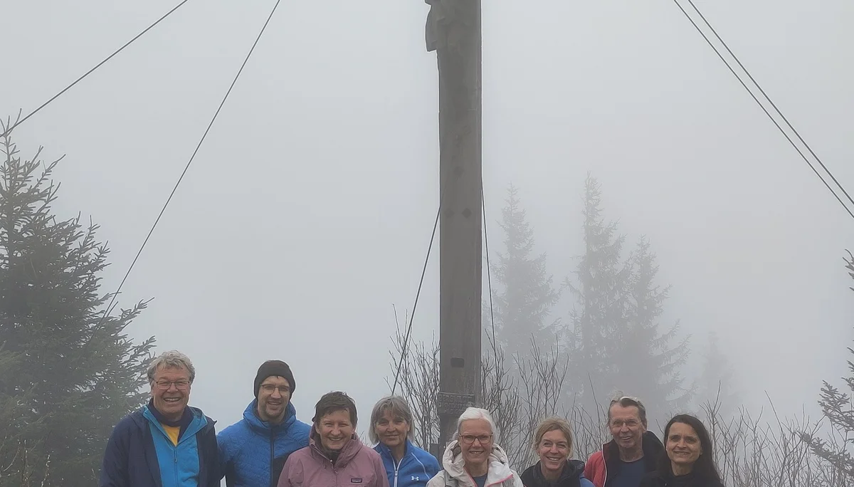 Acht Wanderer stehen nebeneinander vor einem großen Gipfelkreuz am Innenstädter Horn, umgeben von Bäumen. | © Sektion Geltendorf