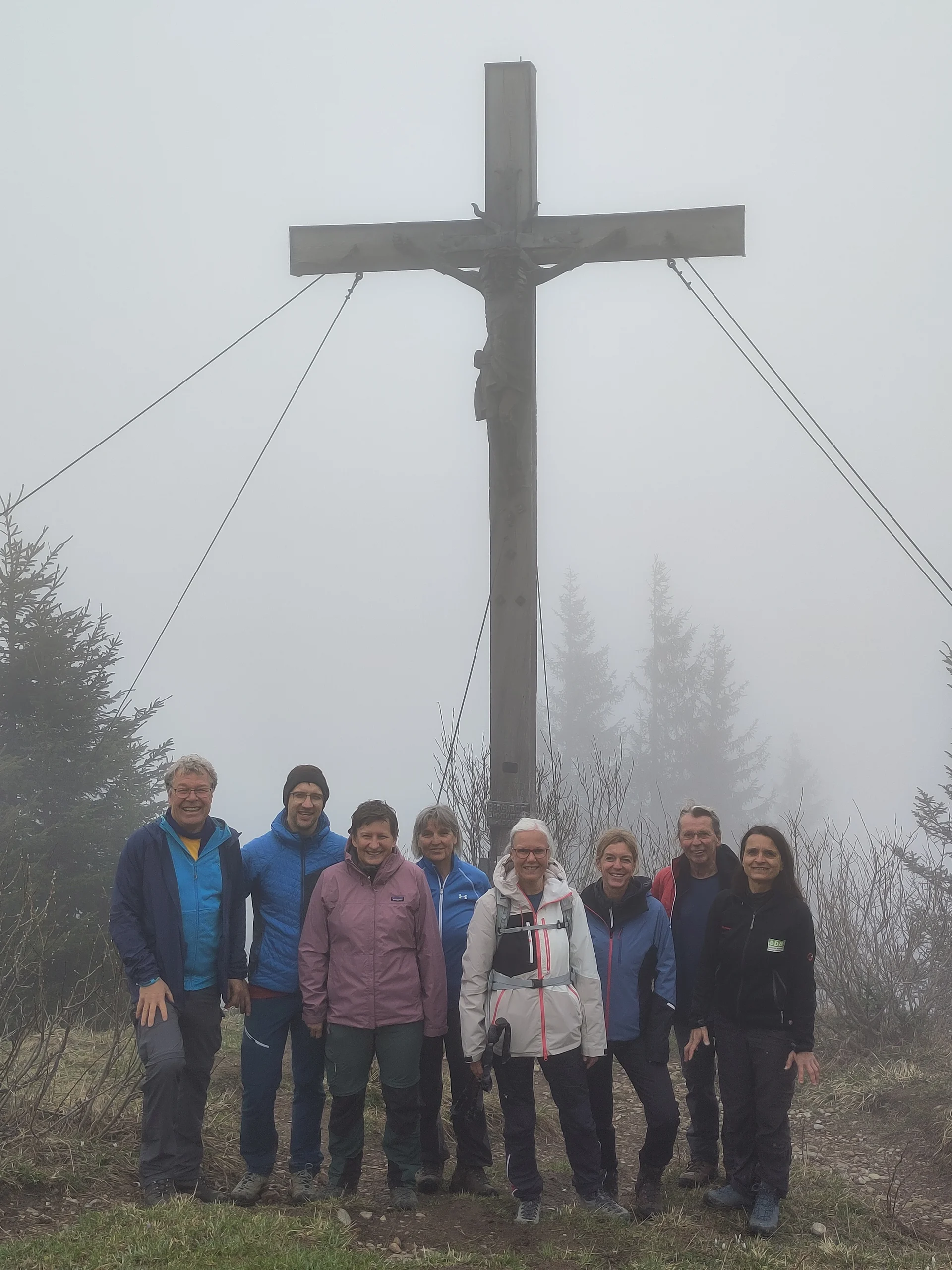 Acht Wanderer stehen nebeneinander vor einem großen Gipfelkreuz am Innenstädter Horn, umgeben von Bäumen. | © Sektion Geltendorf