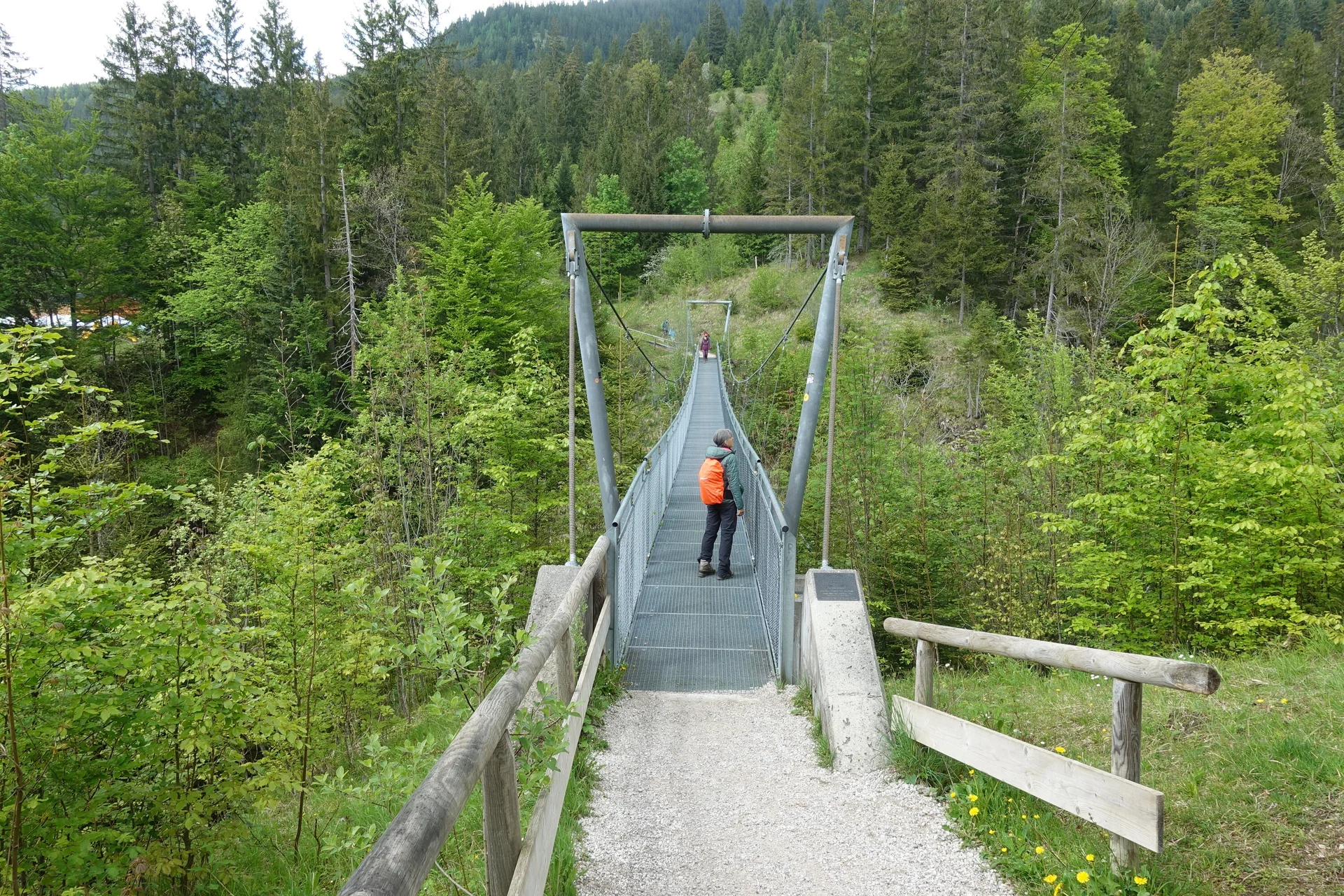 Person mit orangefarbenem Rucksack auf einer schmalen Hängebrücke über einem bewaldeten Tal | © DAV Sektion Geltendorf