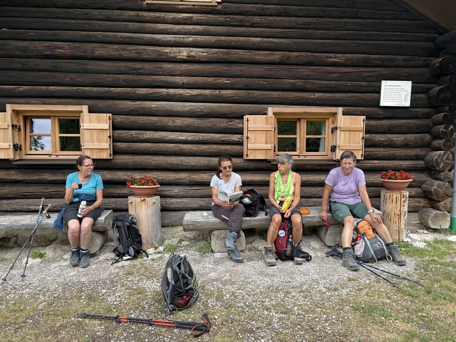 Vier Wanderer sitzen vor einer Holzhütte mit zwei geöffneten Fenstern und Blumentöpfen auf einer Bank und einem Baumstumpf | © DAV Sektion Geltendorf