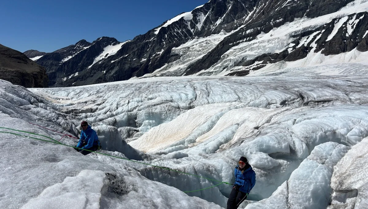 Zwei Personen in blauen Jacken auf einem Gletscher mit tiefen Spalten, umgeben von schneebedeckten Bergen | © Steffen Wolf