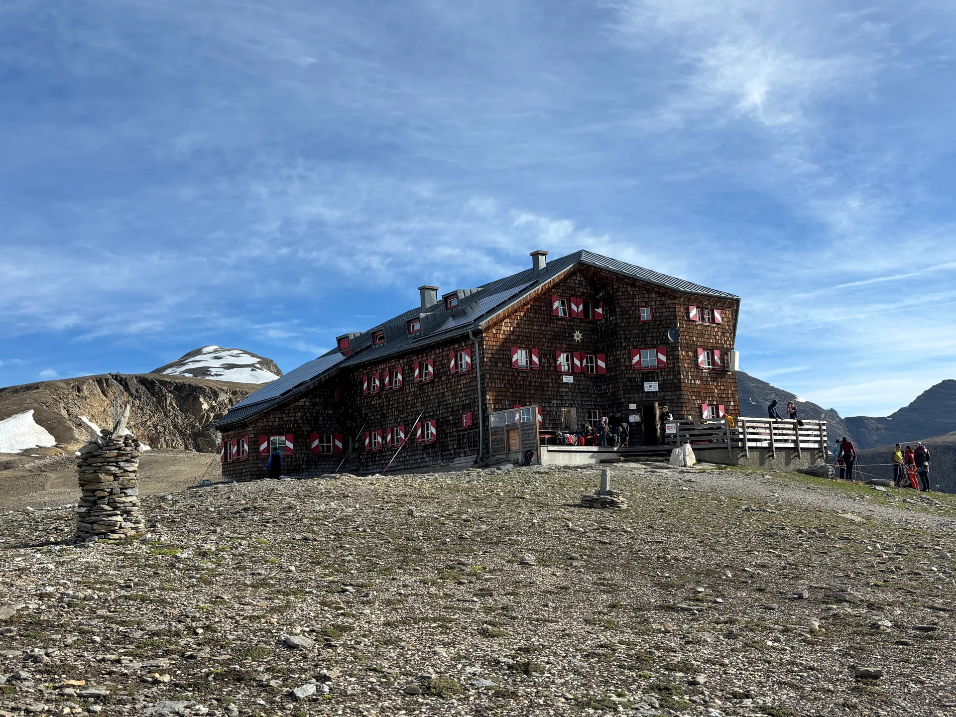 Berghütte mit rot-weiß gestrichenen Fensterläden auf felsigem Gelände unter blauem Himmel, im Hintergrund schneebedeckter Berg | © Steffen Wolf
