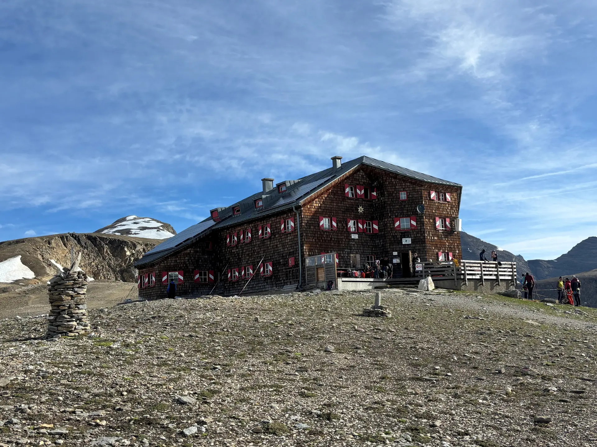 Berghütte mit rot-weiß gestrichenen Fensterläden auf felsigem Gelände unter blauem Himmel, im Hintergrund schneebedeckter Berg | © DAV Sektion Geltendorf