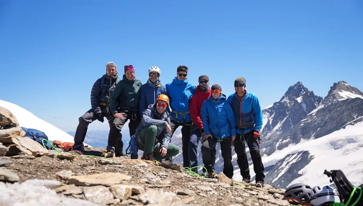 Acht Bergsteiger in Outdoor-Bekleidung posieren auf felsigem Gipfel mit schneebedeckten Bergen im Hintergrund | © DAV Sektion Geltendorf
