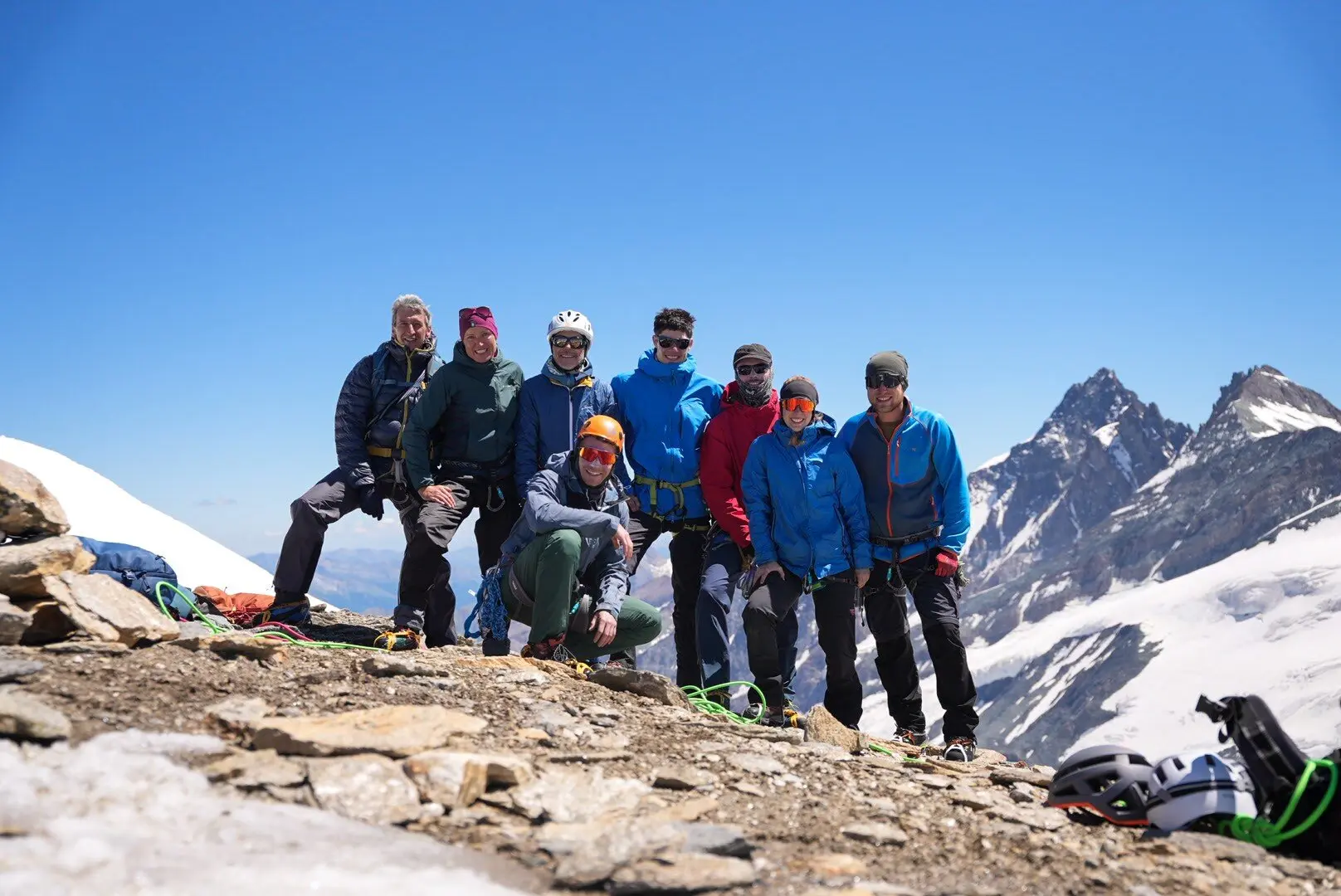 Acht Bergsteiger in Outdoor-Bekleidung posieren auf felsigem Gipfel mit schneebedeckten Bergen im Hintergrund | © DAV Sektion Geltendorf