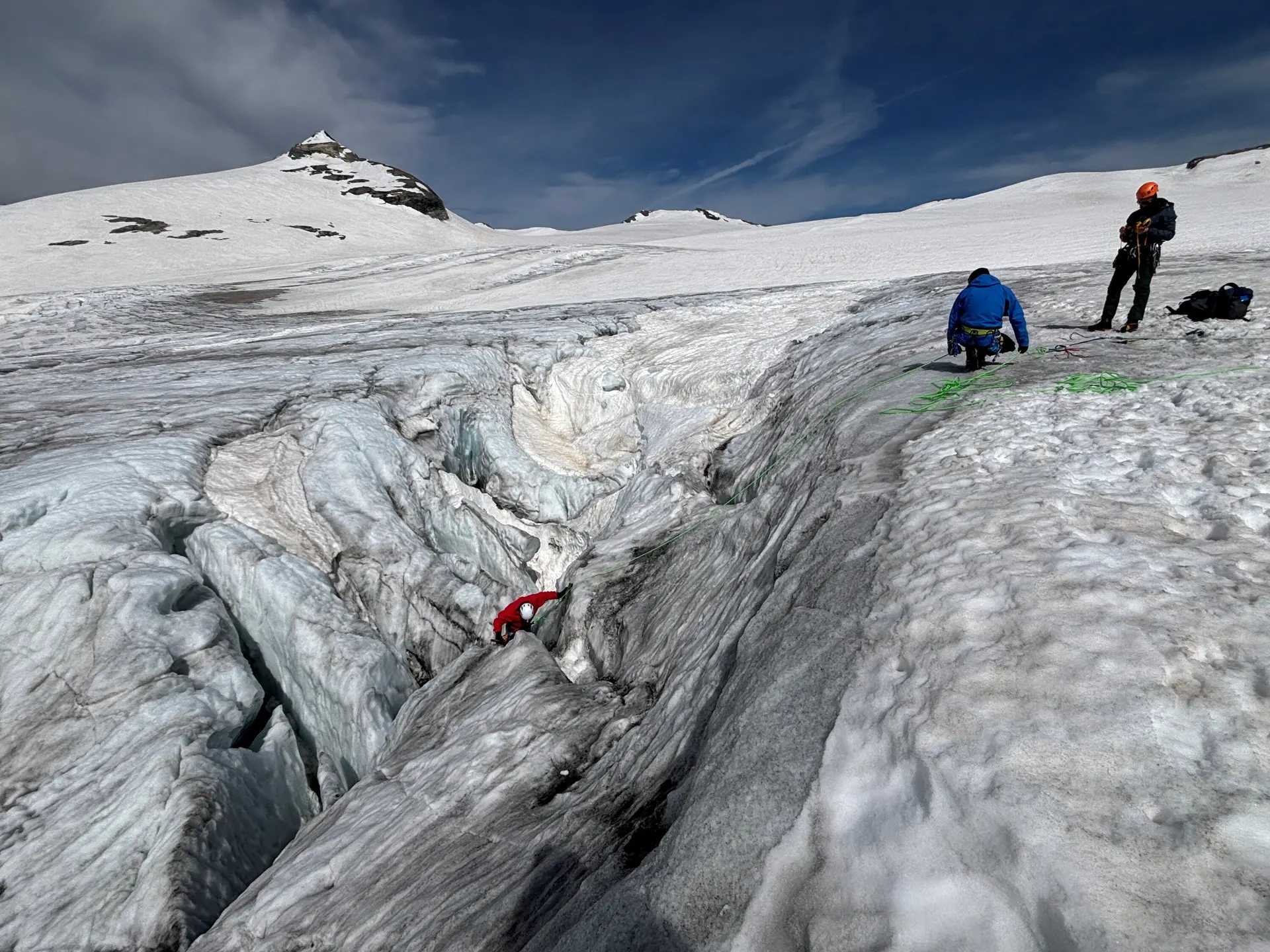 Zwei Personen in Bergsteigerausrüstung auf einem Gletscher neben einer tiefen Spalte, eine Person klettert hinein | © DAV Sektion Geltendorf