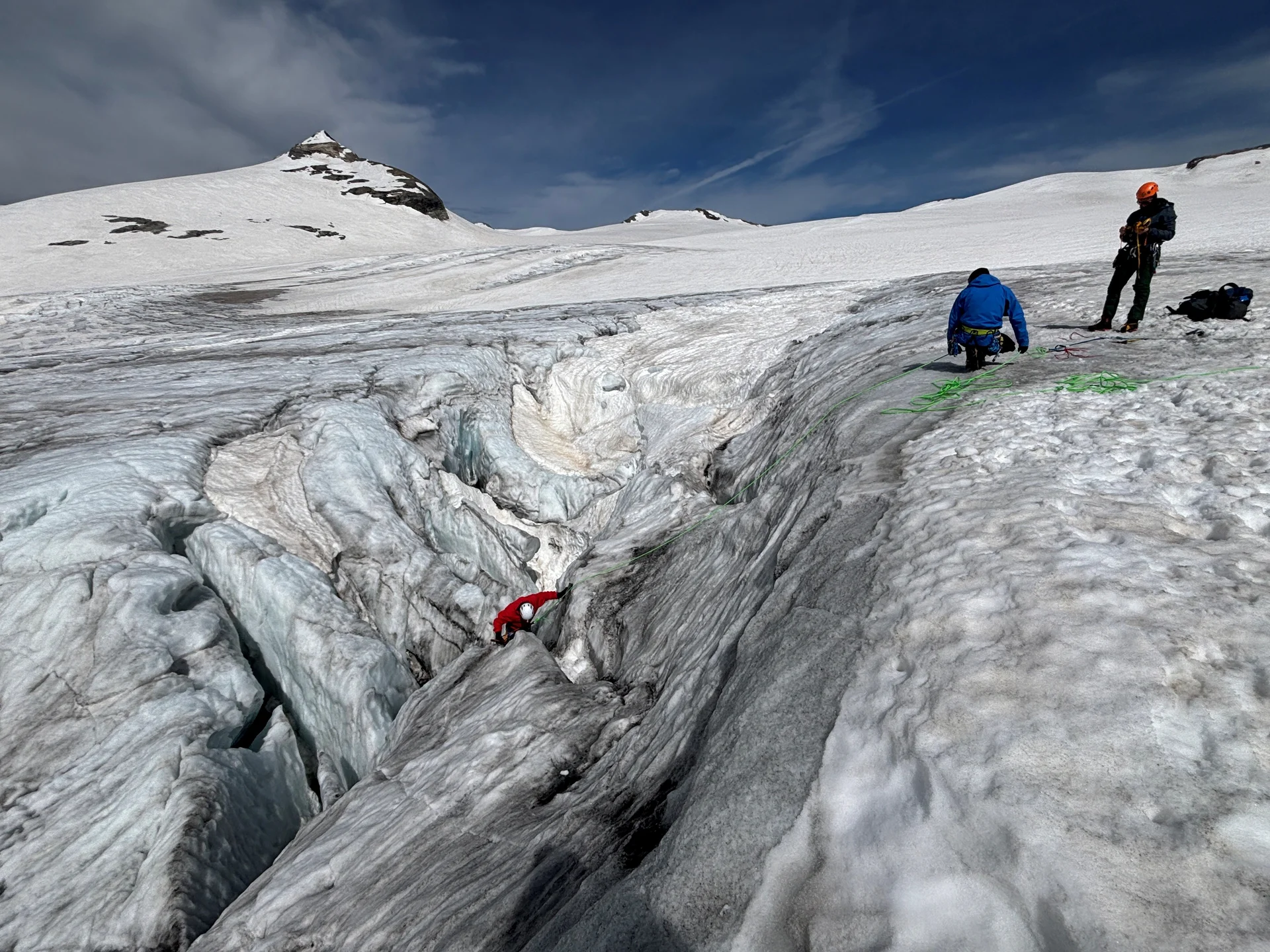 Zwei Personen in Bergsteigerausrüstung auf einem Gletscher neben einer tiefen Spalte, eine Person klettert hinein | © Steffen Wolf