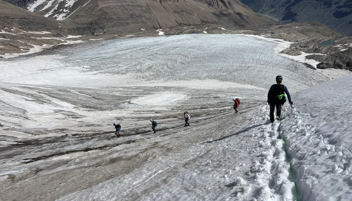 Fünf Bergsteiger steigen in einer Reihe auf einem schneebedeckten Gletscher in den Alpen auf, umgeben von felsigen Bergen | © Steffen Wolf