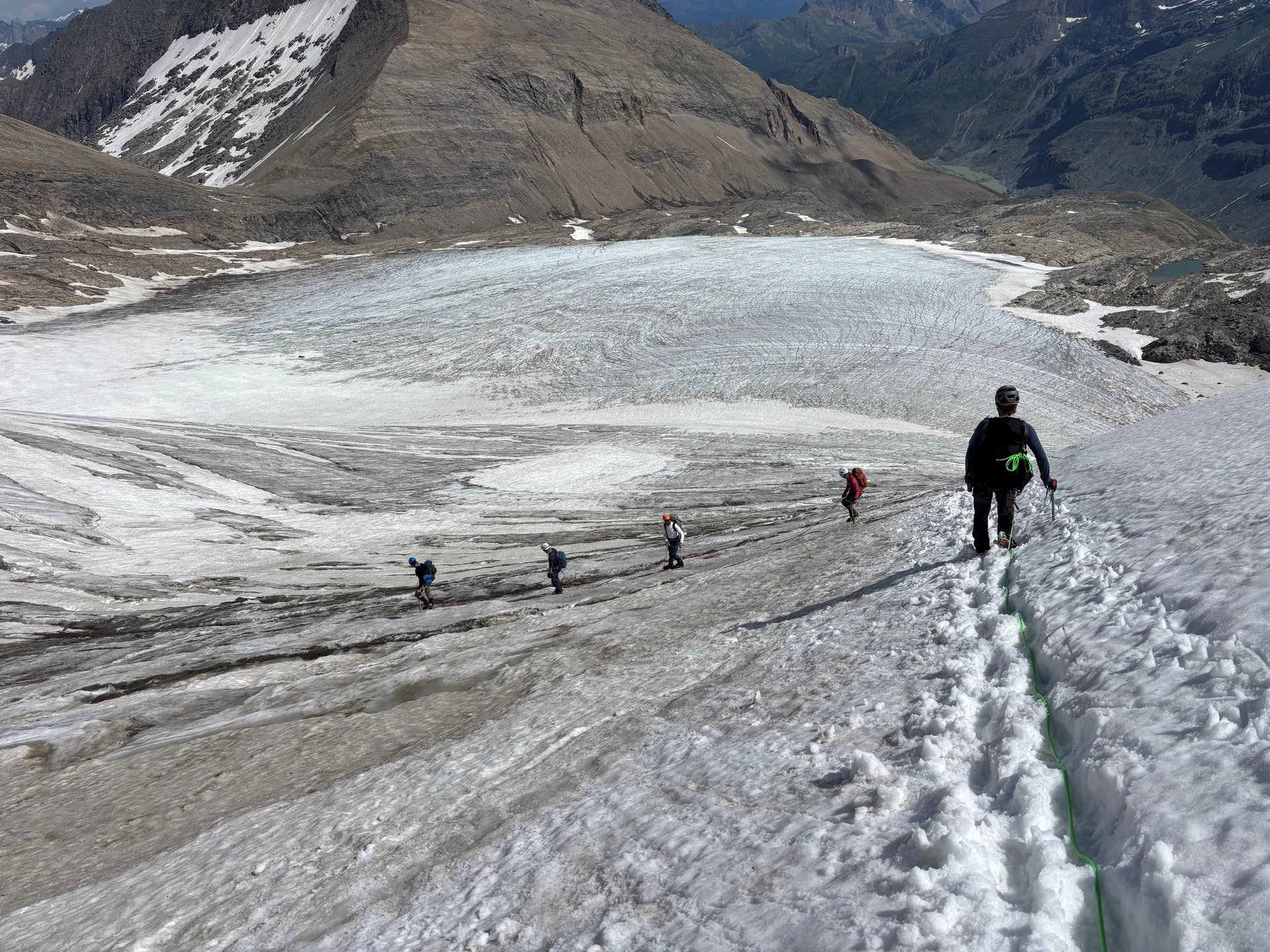 Fünf Bergsteiger steigen in einer Reihe auf einem schneebedeckten Gletscher in den Alpen auf, umgeben von felsigen Bergen | © Steffen Wolf