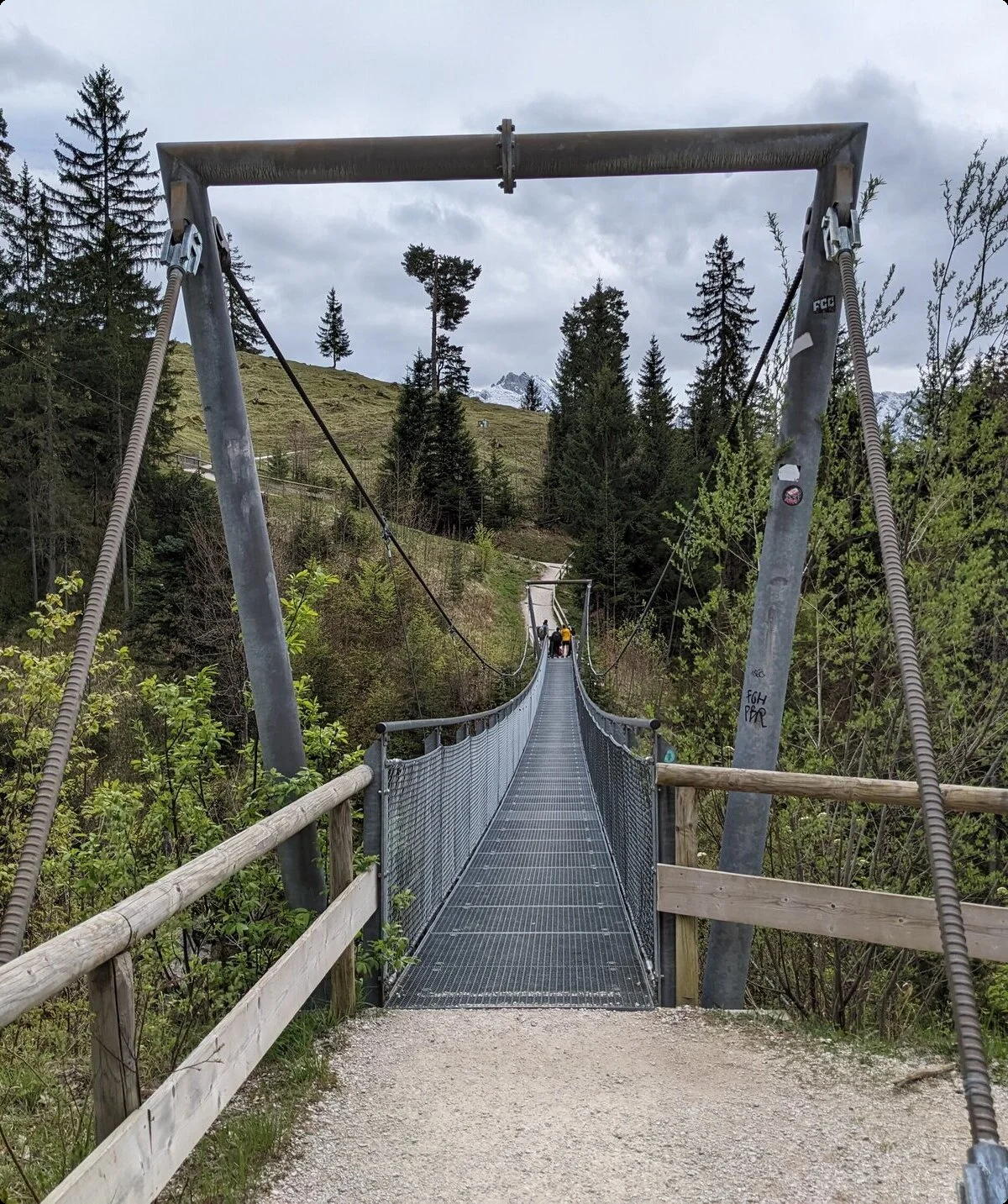 Hängebrücke aus Metall und Holz führt über bewaldetes Tal zu einem Wanderweg im Berggebiet | © DAV Sektion Geltendorf