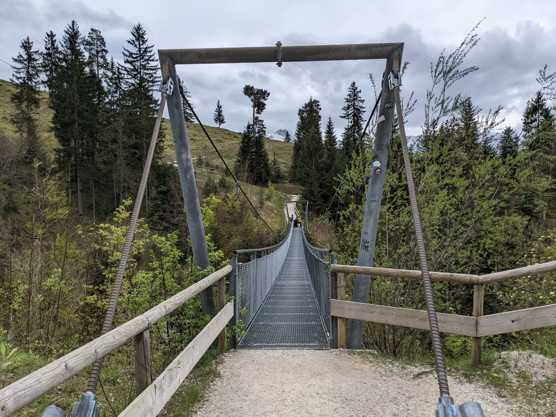 Hängebrücke aus Metall und Holz führt über bewaldetes Tal zu einem Wanderweg im Berggebiet | © DAV Sektion Geltendorf