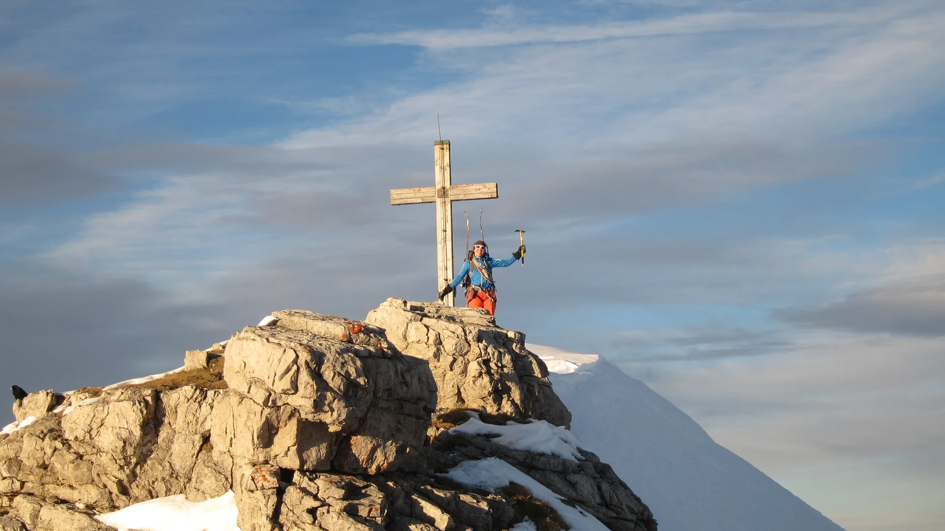 Bergsteiger steht auf Felsen neben einem Gipfelkreuz | © DAV Sektion Geltendorf