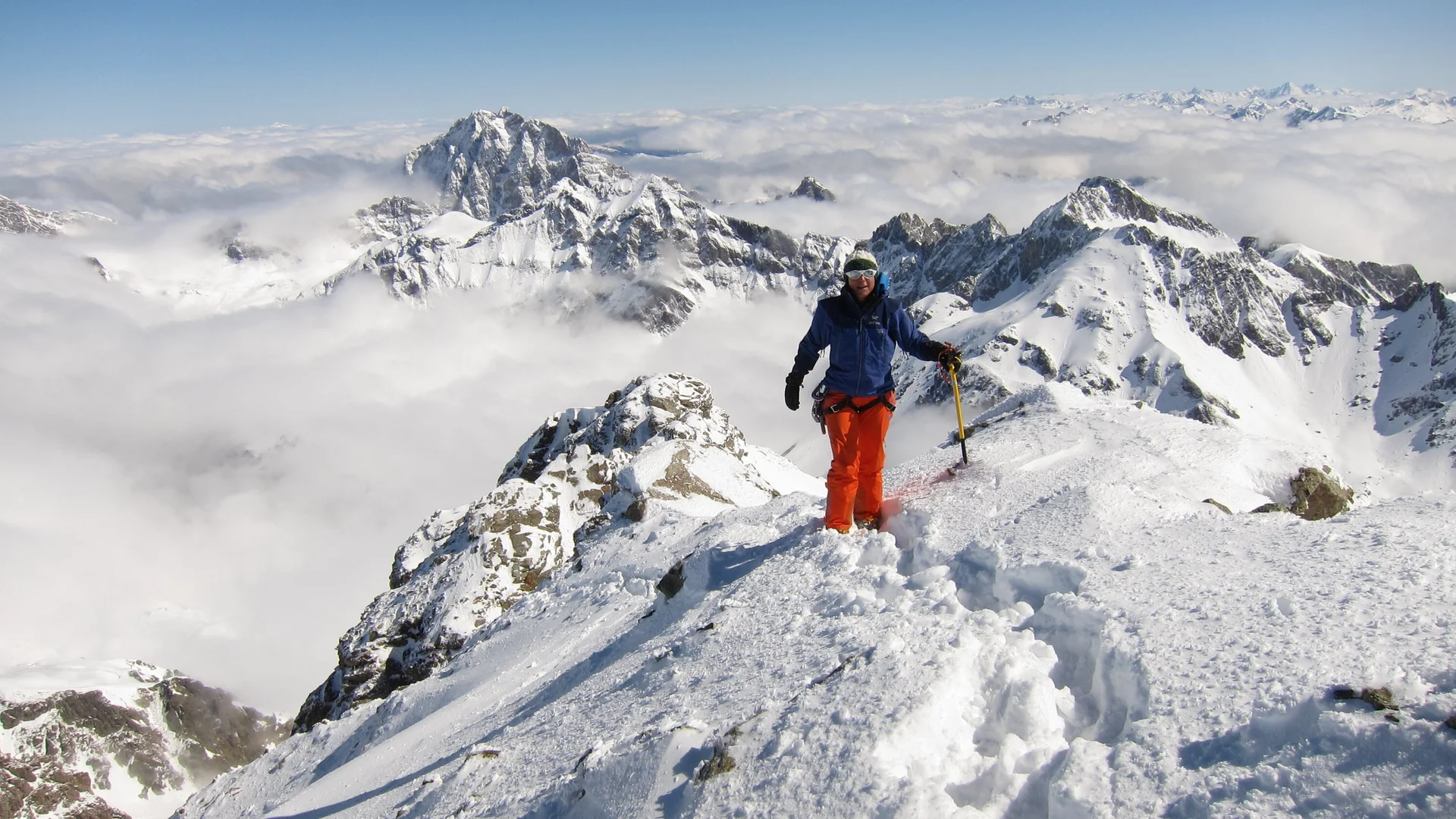 Bergsteiger steht mit Eispickel auf schneebedecktem Gipfel mit Bergpanorama und Wolken darunter | © DAV Sektion Geltendorf Bergsteiger steht mit Eispickel auf schneebedecktem Gipfel mit Bergpanorama und Wolken darunter | © DAV Sektion Geltendorf
