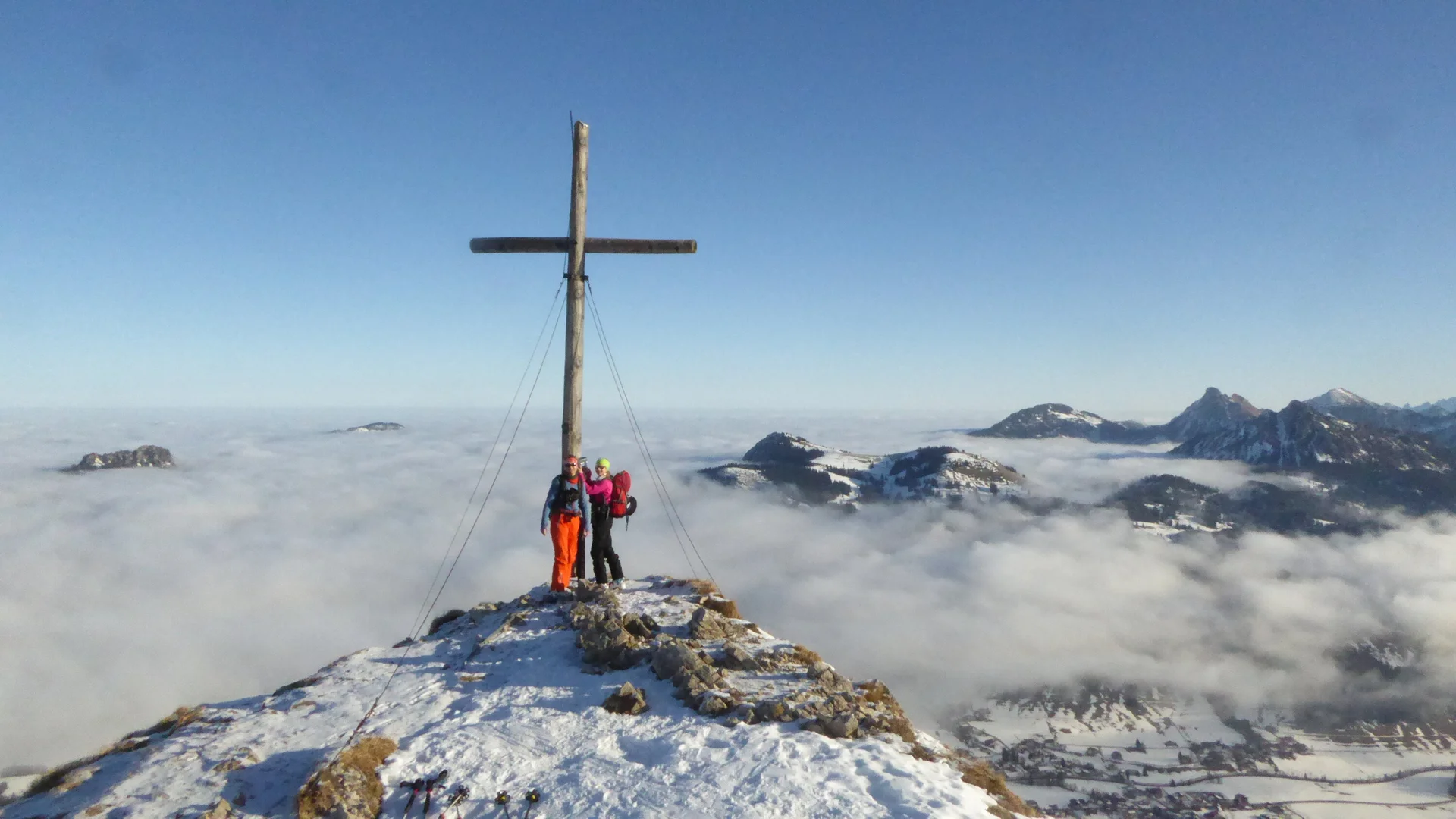 Zwei Wanderer stehen am Gipfelkreuz Kühgundkopf auf schneebedecktem Berggipfel  | © DAV Sektion Geltendorf