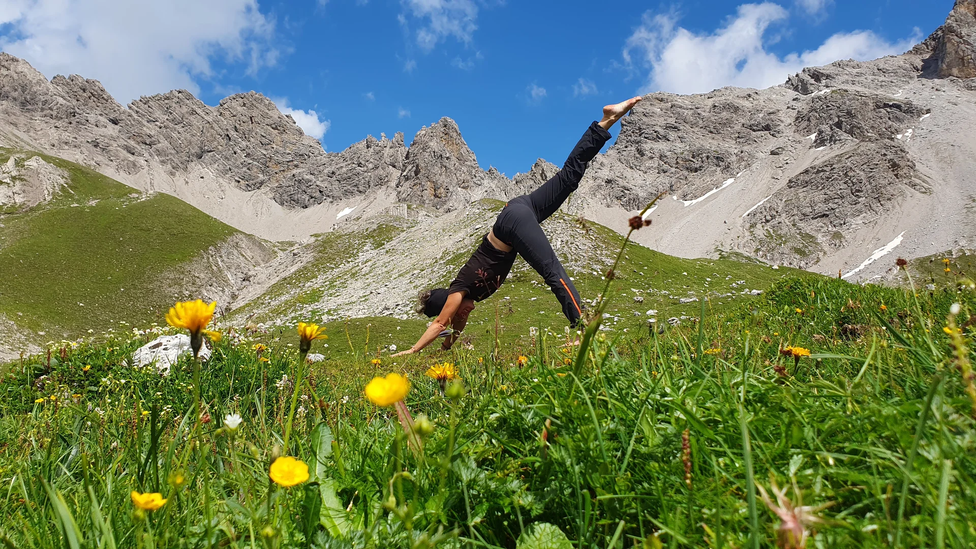 Yoga-Pose auf grüner Bergwiese mit gelben Blumen vor felsigen Bergen | © DAV Sektion Geltendorf