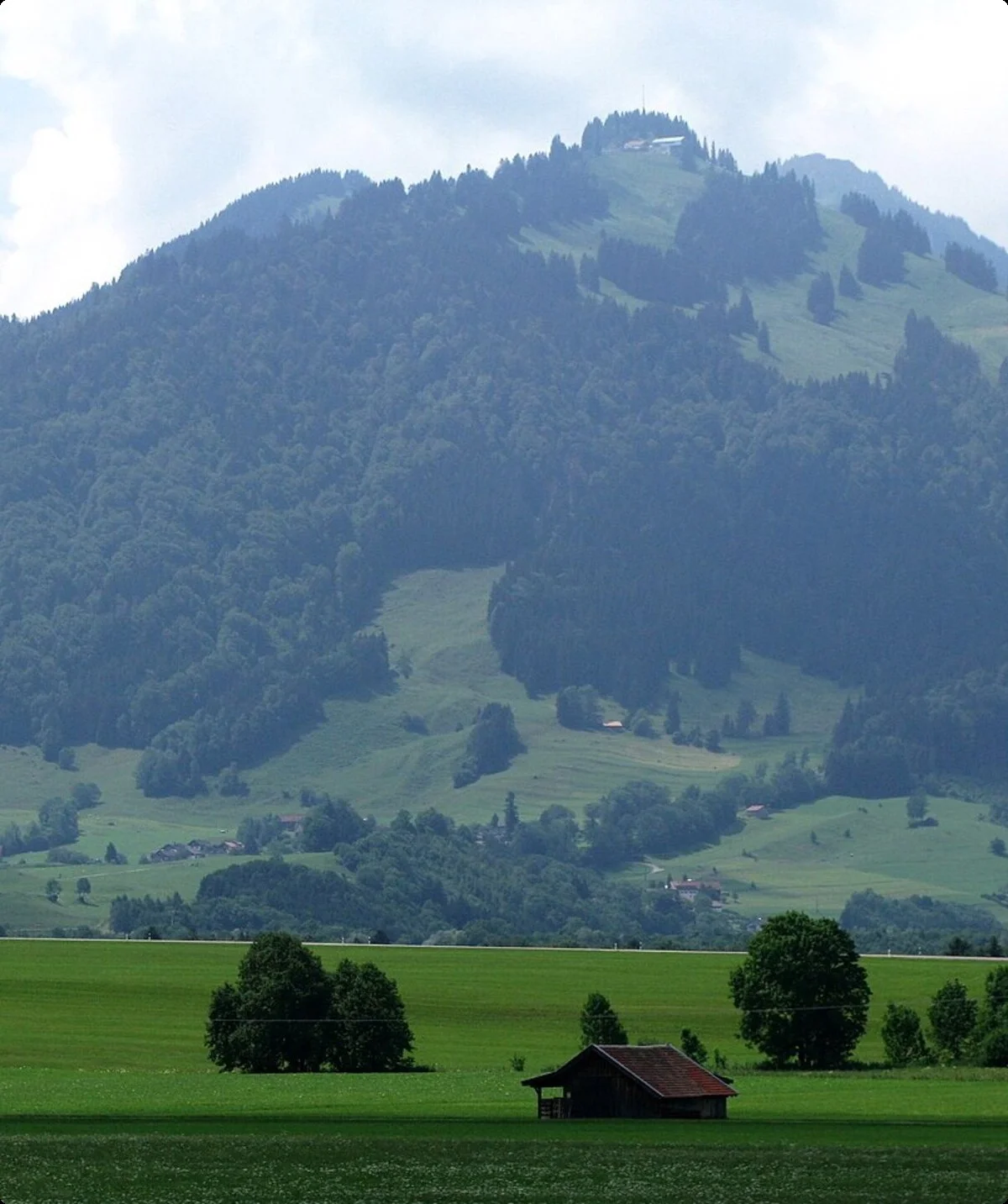 Berg Fockenstein mit bewaldeten Hängen und grünen Wiesen im Vordergrund, vereinzelt kleine Holzhäuser | © DAV Sektion Geltendorf
