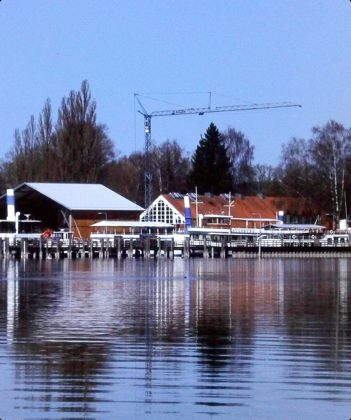 Hafen mit Stegen und Gebäuden am Ufer des Ammersees, ruhiges Wasser spiegelt die Szenerie | © Hartmut Engel