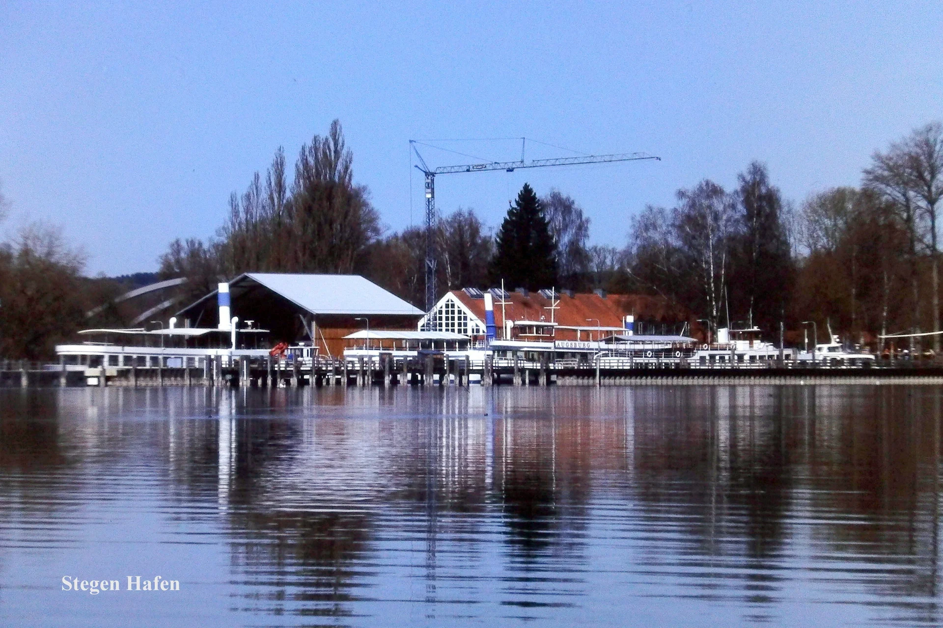 Hafen mit Stegen und Gebäuden am Ufer des Ammersees, ruhiges Wasser spiegelt die Szenerie | © Hartmut Engel
