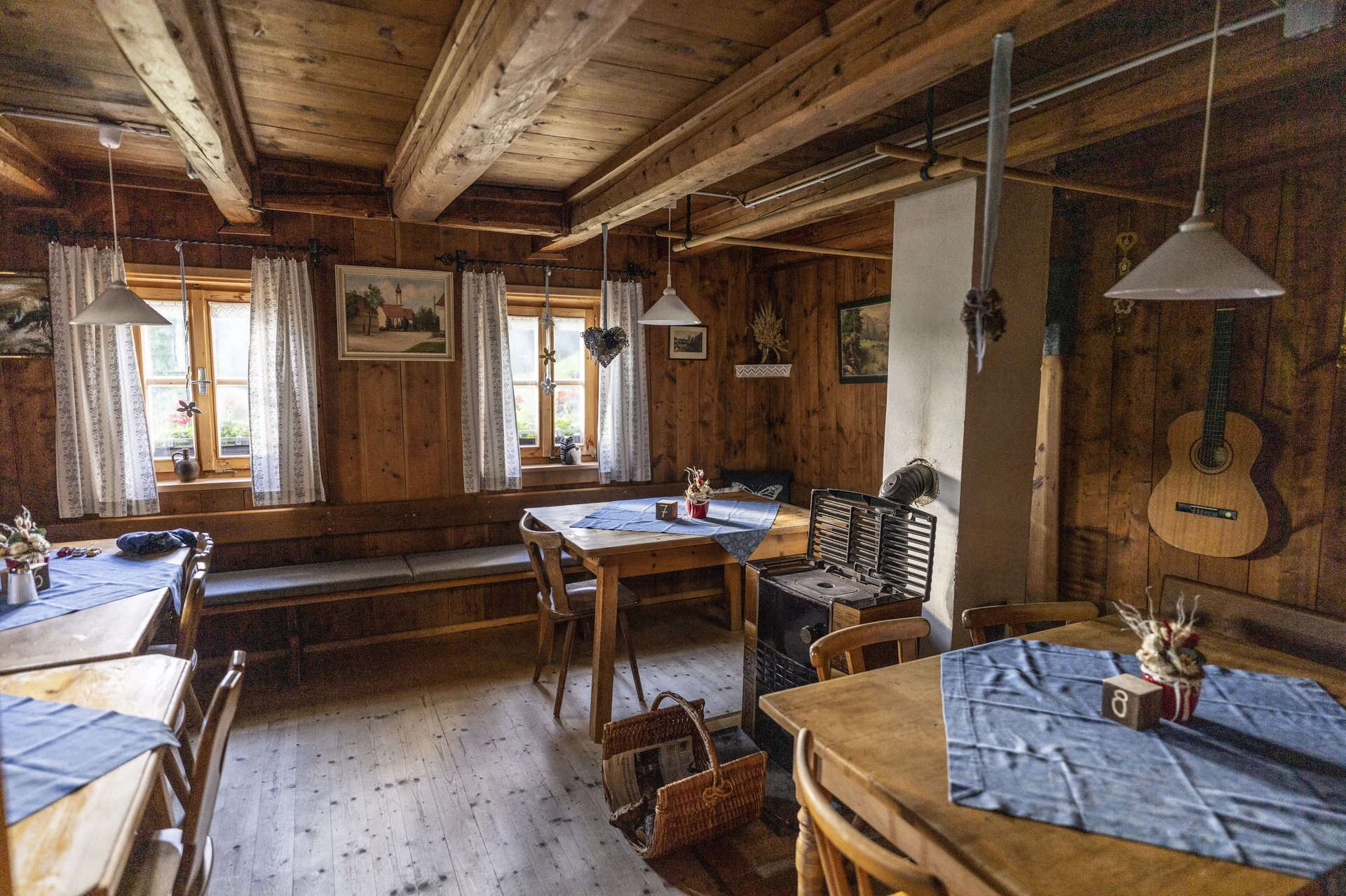 Gemütlicher Gastraum der Neuen Magdeburger Hütte mit Holztischen, blauen Tischdecken, Holzverkleidung und einer an der Wand hängenden Gitarre | © DAV/Wolfgang Ehn
